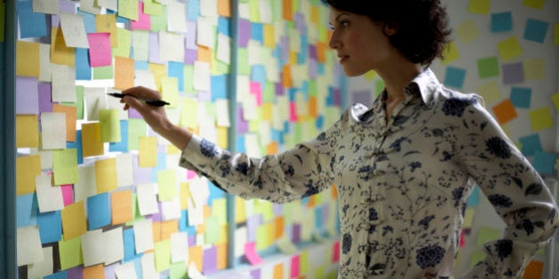 Woman writing on wall covered with adhesive notes