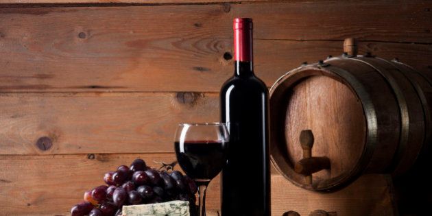 Wine bottle with glass, bunch of grapes, blue cheese, walnuts and wooden barrel on old wooden background