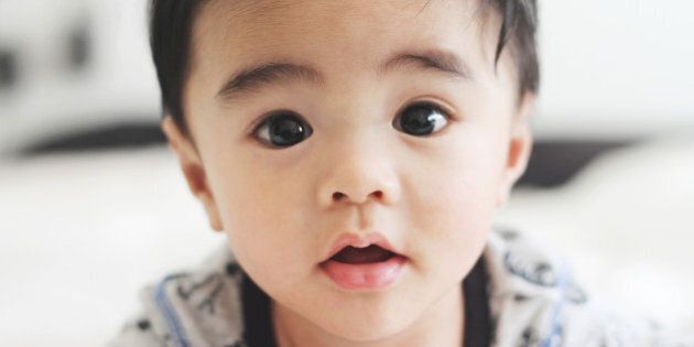 Closeup photo of five month old baby boy (Asian/Filipino) on his tummy staring at the camera. He has a heart shaped mouth.
