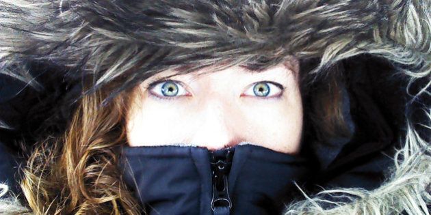 Close up of woman's face, focused on green eyes, zipped inside the hood of a large winter coat or parka, with a fur lining. Cold weather portrait.