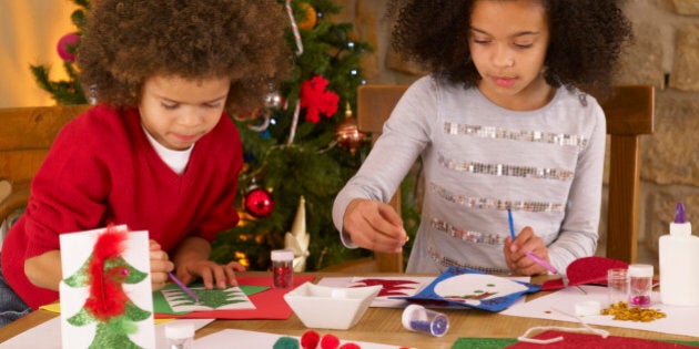 Mixed race children making Christmas cards with glitter and feathers on dining room table