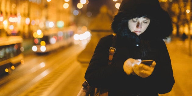 Woman in winter clothing texting in an urban scene.