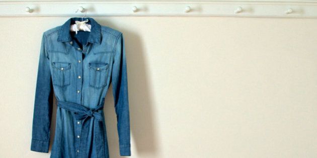 Weathered denim dress with pearl buttons hanging against plain white wall.