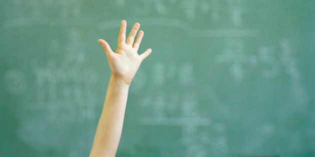 Female student (12-14) raising hand in classroom, close-up
