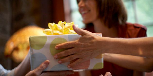 Two women exchanging gift over table, close-up of hands, out of focus woman in background