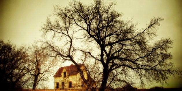 Spooky abandoned farm house overshadowed by large trees, Alberta