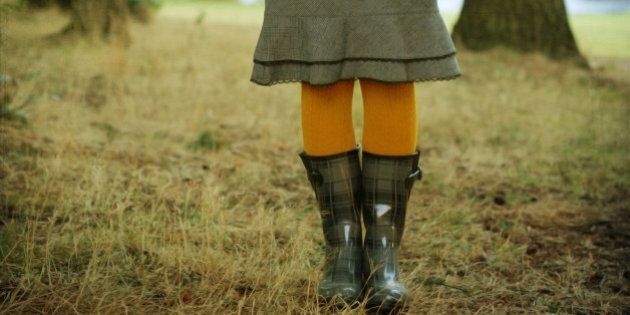 Woman wearing gray rainboots and yellow tights in forest clearing.