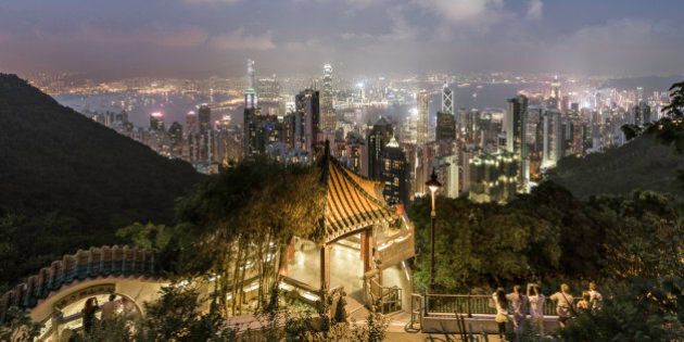 China,Hong Kong, tourists admiring the skyline from Victoria peak, at dusk, standing next to a viewing point with traditional architecture.