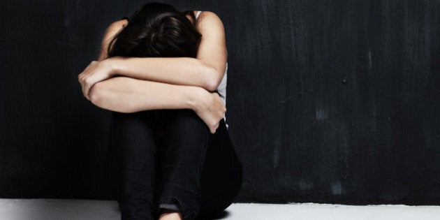 A studio shot of an emotionally distressed young woman sitting on the floor with her head in her arms