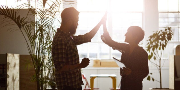 Creative coworkers doing high five at the office, in the sunset