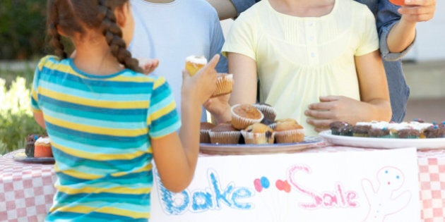 Group Of Children Holding Bake Sale With Mother Smiling And Laughing.