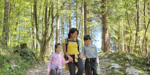 Mother holding her children's hands, walking and chatting happily in the forest.