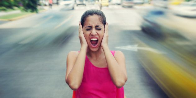 Portrait of woman standing still in the middle of a street with cars passing by fast, screaming stressed and frustrated