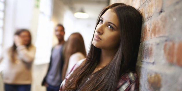 Shot of a bored-looking student standing in a hallway with her classmates in the background