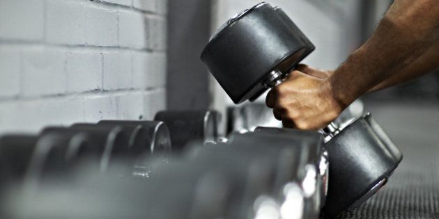 Strong black male picking up dumbbells from selection of free weights in gym, ready for workout