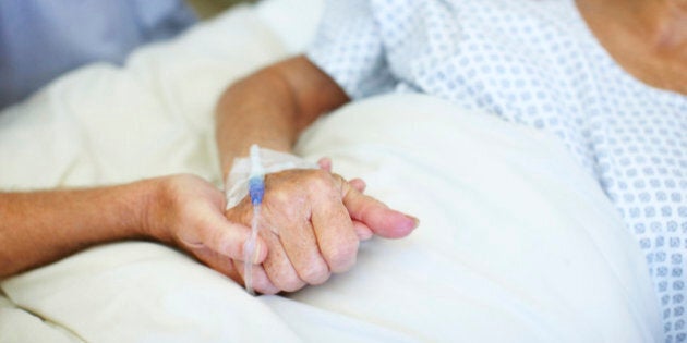 Closeup shot of an elderly man holding his wife's hand while she is ill in the hospital