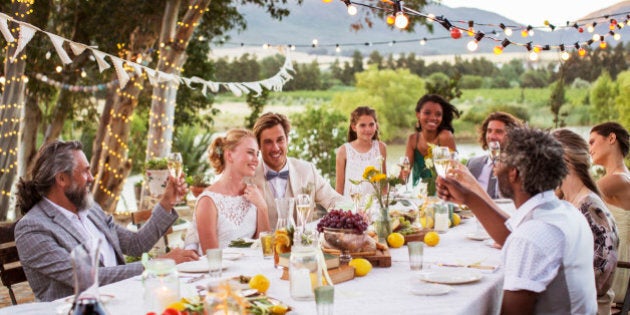 Young couple and their guests sitting at table during wedding reception in garden