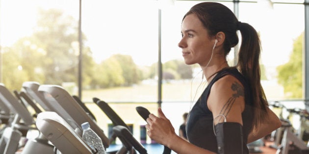 Woman in a gym on a running machine, she has headphones in a smartphone in an arm older