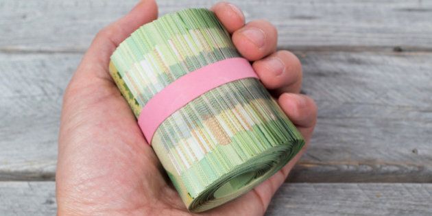 Hand holding a roll of green bank notes against wooden table