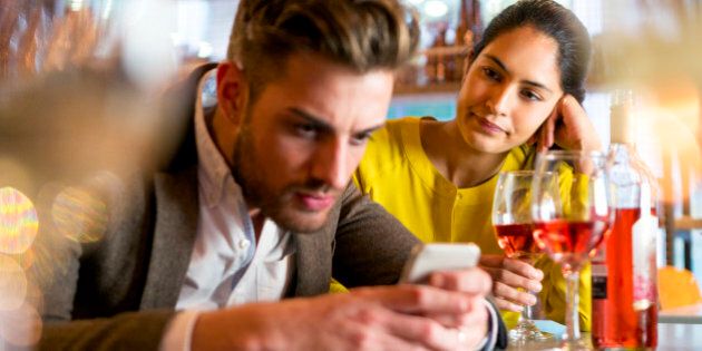 A couple are out having drinks and the woman looks irritated that her partner is on his mobile phone and not paying her any attention.