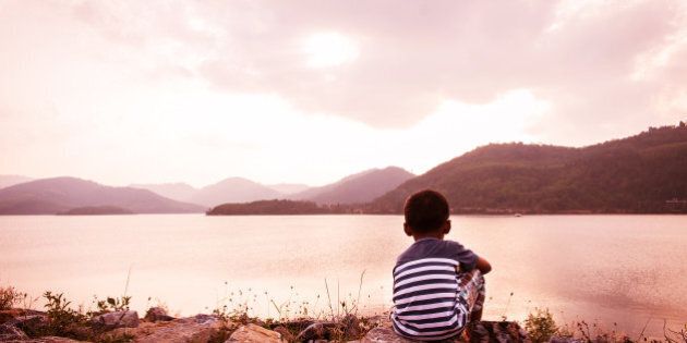 little boy sitting alone at dam in the evening