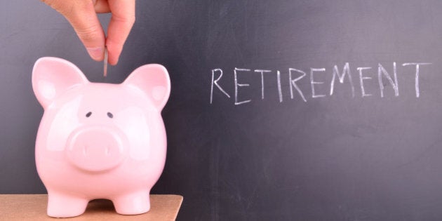 Depositing coins and money into a pink piggybank with retirement written in white chalk on a blackboard