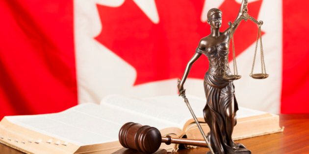 Lady justice, gavel and a law book against the national flag of Canada.