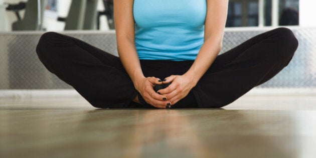 Young woman in a gym looking forward preforming a groin stretching exercise. Horizontal shot.