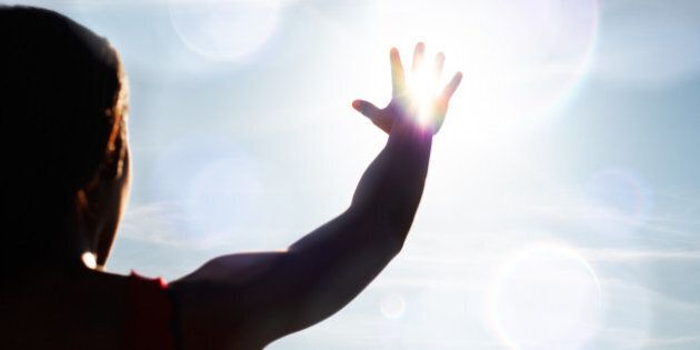 Young woman reaching for the sun, with flare.