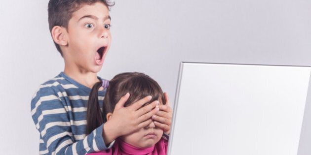 Little boy protects his sister from watching inappropriate content while using a computer. Internet safety for kids concept. Toned image with selective focus