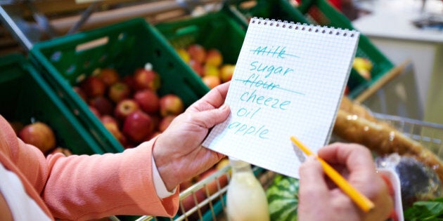 Image of senior woman hands holding product list with goods in cart near by