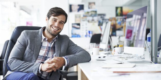 Portrait of happy businessman sitting at desk in creative office