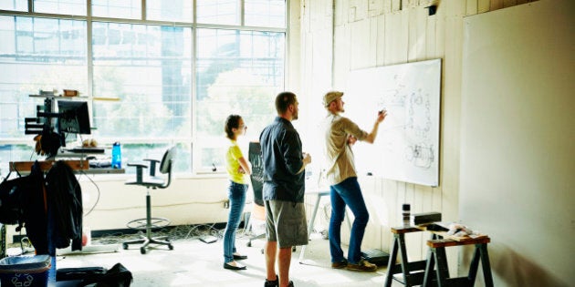 Engineer sketching project plans on whiteboard with coworkers in workshop