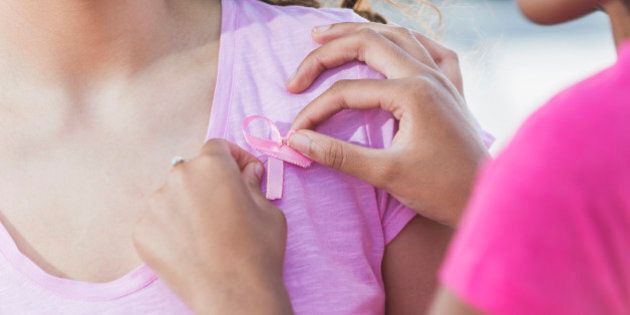 Cropped, close up view of two multi-ethnic teenage girls participating in a breast cancer awareness rally. An African American 14 year old teenager is pinning a pink ribbon on her friend's shirt.