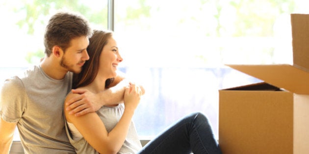 Happy couple hugging moving new house sitting on the floor and looking through the window