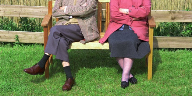 Elderly couple sitting on bench outdoors, low section