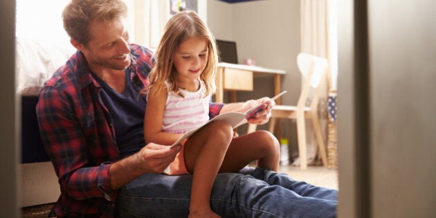 Father and young daughter reading together in bedroom