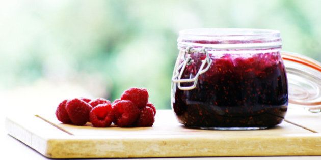 Delicious home-made raspberry jam in a jar and fresh raspberries on the side.