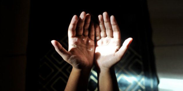 A muslim woman making dua(prayers) as light falls on her palm.