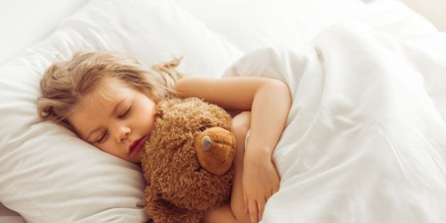 Sweet little girl is hugging a teddy bear while sleeping in her bed at home