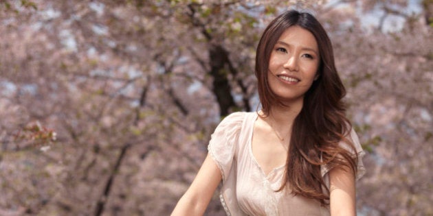 Young smiling Asian Woman riding a bicycle in a park past blooming cherry trees