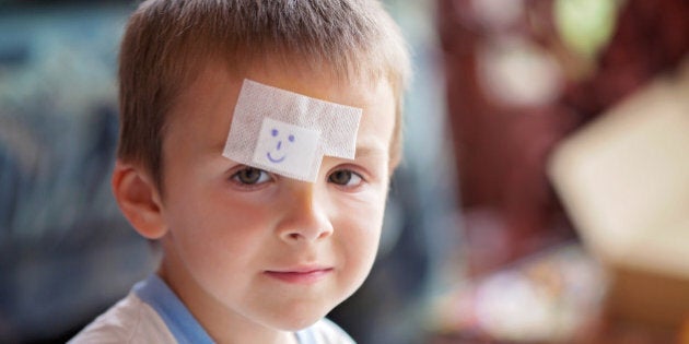 Close portrait of a boy with band aid on forehead, injured, sad but smiling