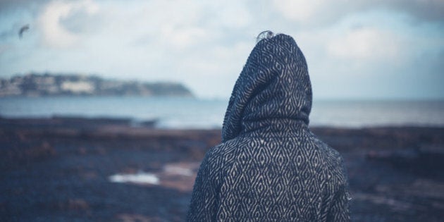 A young woman wearing a hooded coat is walking on a dramatic beach in the winter