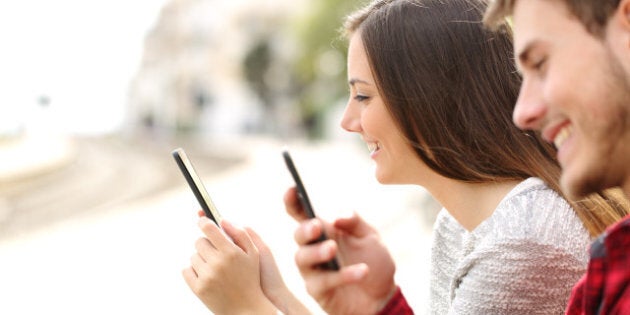 Happy teen couple using smart phones in a train station while they are waiting