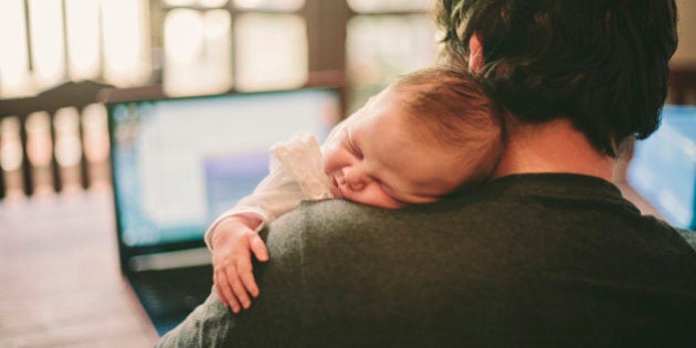Father working on his laptop while his newborn baby girl sleeps on his shoulder