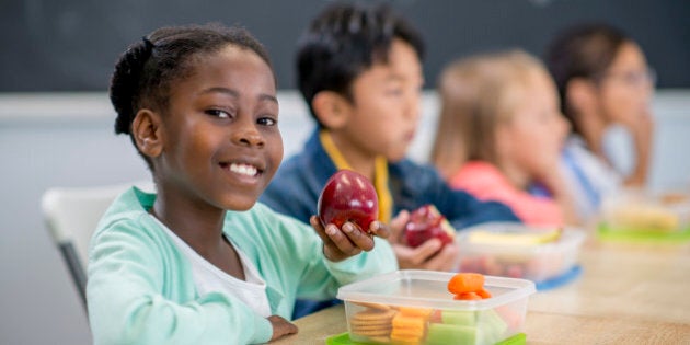 A multi-ethnic group of elementary age children are sitting at their desks and are eating their healthy lunches.