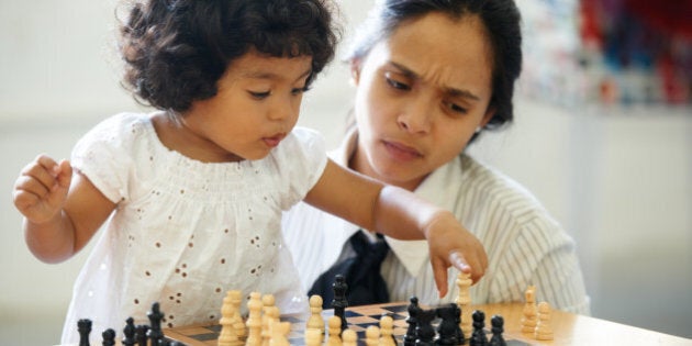 A cute little girl playing chess while her mom looks confused