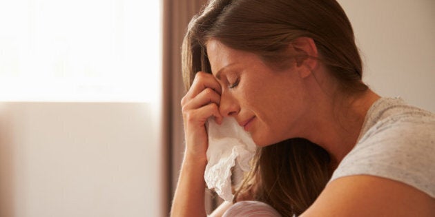 Woman Suffering From Depression Sitting On Bed And Crying