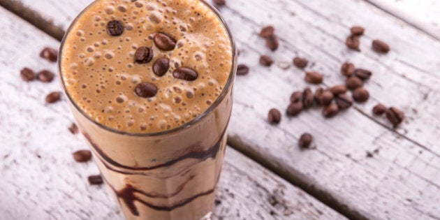 Cold chocolate milkshake frappe in tall glass with ice on white wood background