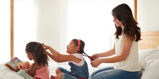 Mother & 2 kids doing each others hair on a row in bed, at sunset